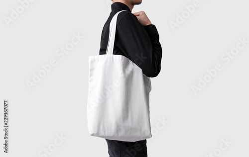 Man is holding bag canvas fabric for mockup blank template isolated on gray background.