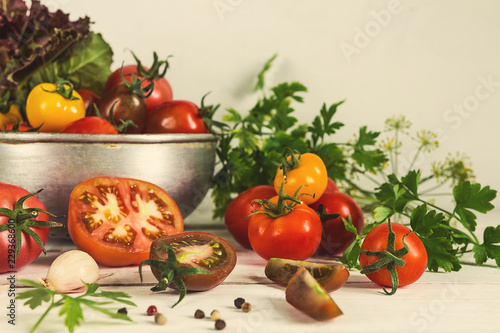 Fresh vegetables tomatoes of different varieties of red yellow in a metal bowl drushlag on a light rustic table, in rustic style tinted horizontal