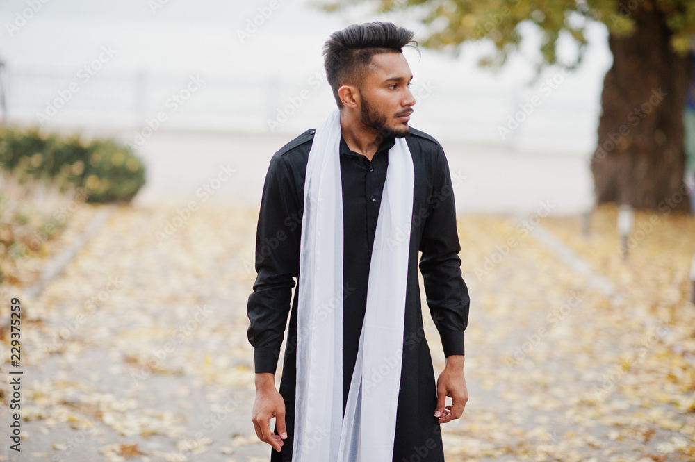 Indian stylish man in black traditional clothes with white scarf posed outdoor against autumn leaves tree. Indian stylish man in black traditional clothes with white scarf posed outdoor against autumn leaves tree.