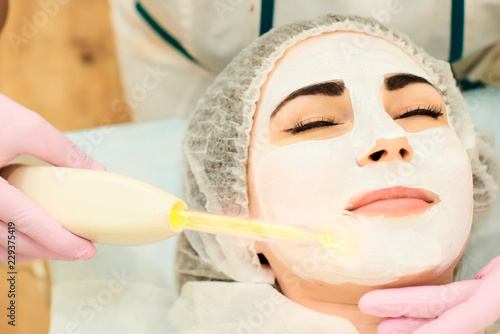 a girl with a white mask on her face is cleaned with a current in the medical office