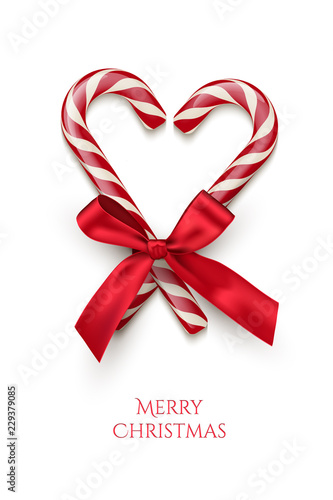 Two red striped candy cane in heart shape with red bow and Merry Christmas text isolated on white background. Vector Christmas design element.