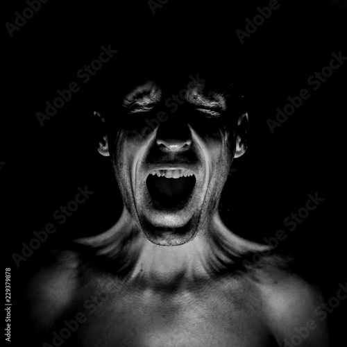 Stylish dark portrait of screaming adult caucasian man. Fear concept. Black and white shot, low key lighting.