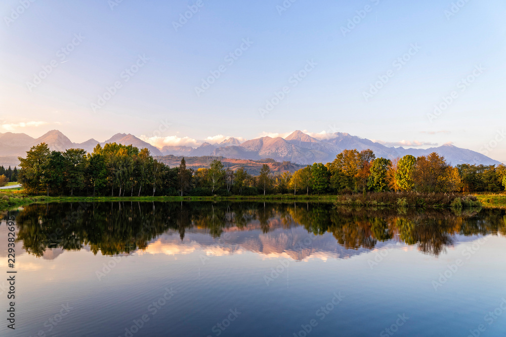 Peaceful scene of beautiful autumn mountain landscape with lake, colorful trees and high peaks. Colorful autumn foliage casts its reflection on the calm waters.