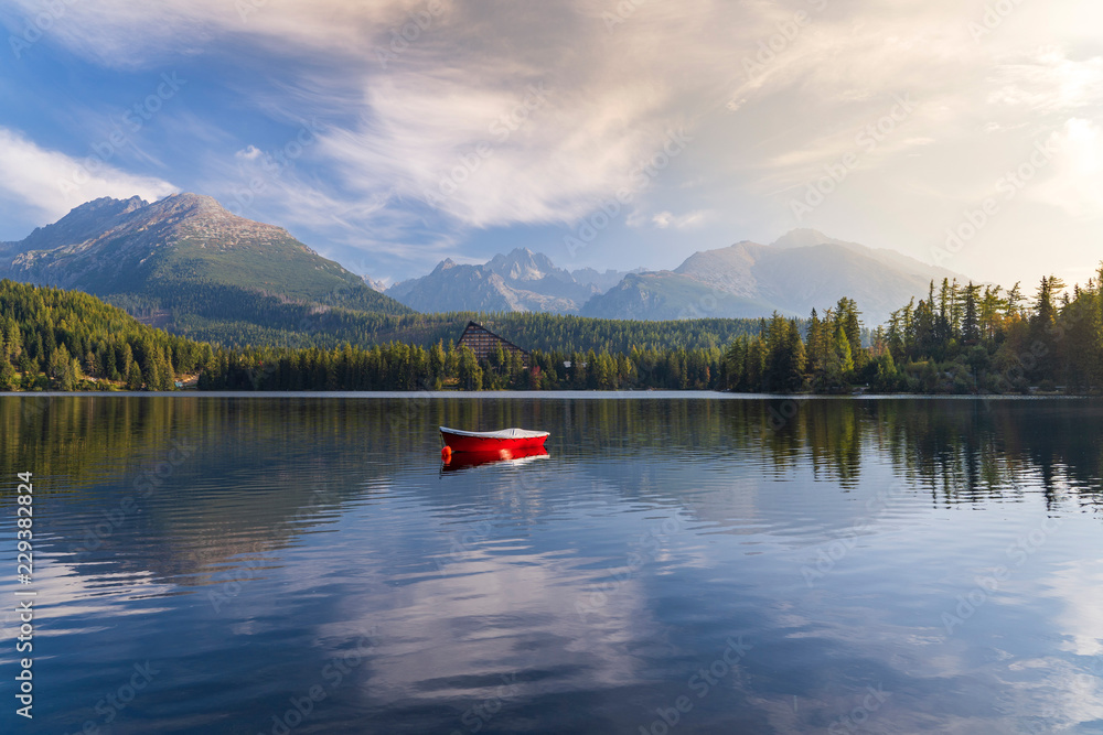 Obraz premium Peaceful mountain scene with mountain hotel next to a lake with boat. Scenic view of Strbske Pleso, High Tatras National Park, Slovakia.