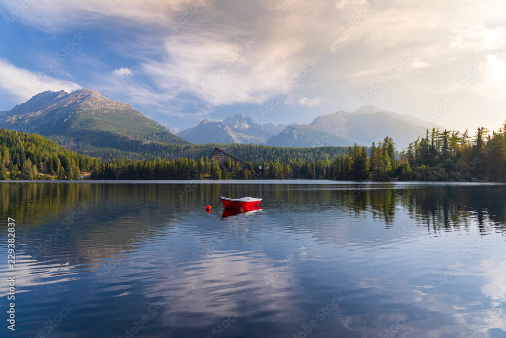 Obraz premium Peaceful mountain scene with mountain hotel next to a lake with boat. Scenic view of Strbske Pleso, High Tatras National Park, Slovakia.