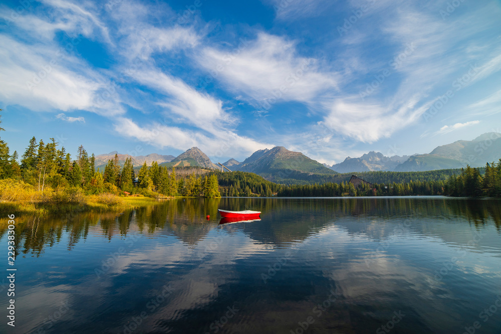 Obraz premium Peaceful mountain scene with mountain hotel next to a lake with boat. Scenic view of Strbske Pleso, High Tatras National Park, Slovakia.