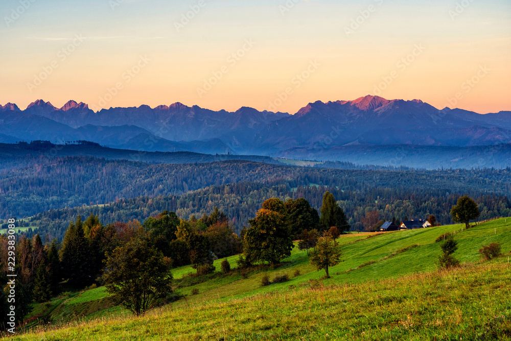 Beautiful sunrise over green meadows and settlement in front of high rocky peaks in High Tatras mountains in a background on Slovak and Polish border.