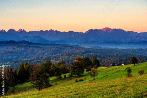 Beautiful sunrise over green meadows and settlement in front of high rocky peaks in High Tatras mountains in a background on Slovak and Polish border.