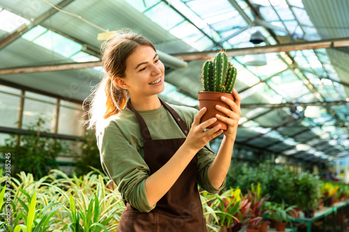 Gardener holding plant cactus standing near flowers in greenhouse