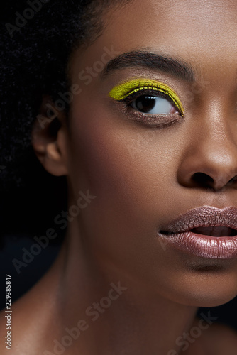 Leinwand Poster partial view of african american model with bright neon eye shadow isolated on b