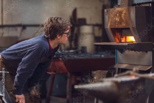 Young blaksmithor metalworker watching a burning furnace