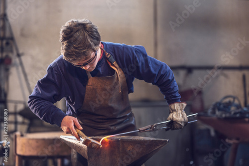 Young blacksmith working with red hot metal Fototapet