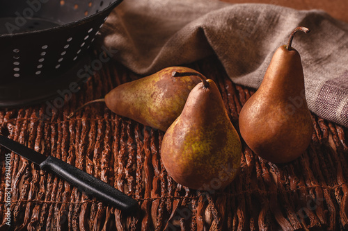 Still life scene of three pears, a paring knife, colander and towel on a woven twig background. photo