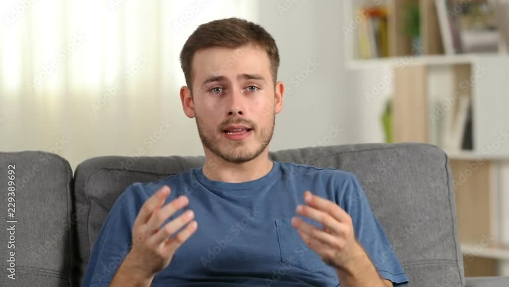 Happy man talking to camera sitting on a couch in the living room at home Happy man talking to camera sitting on a couch in the living room at home