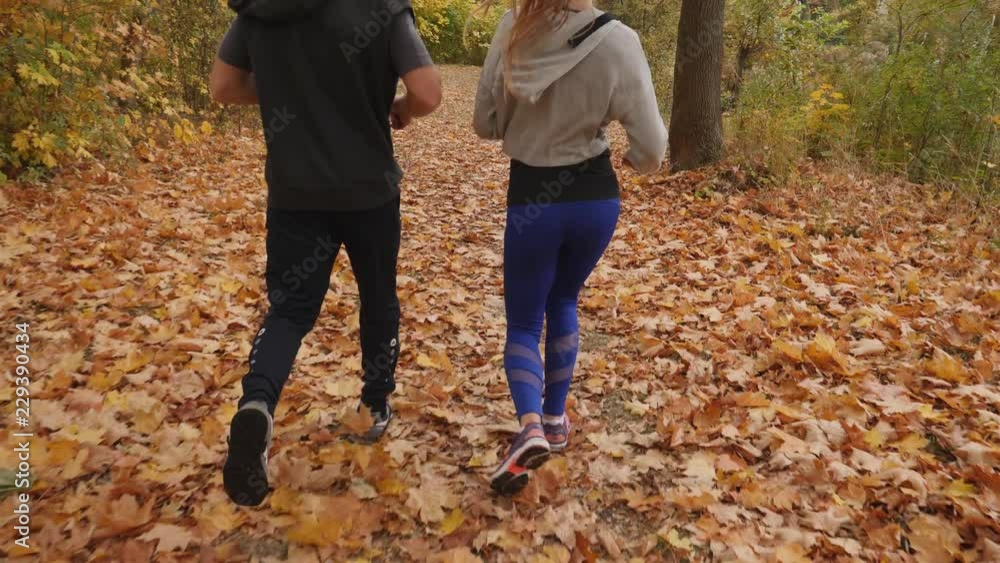 Young people couple sport running together on nature autumn park with fallen leaves Young people couple sport running together on nature autumn park with fallen leaves