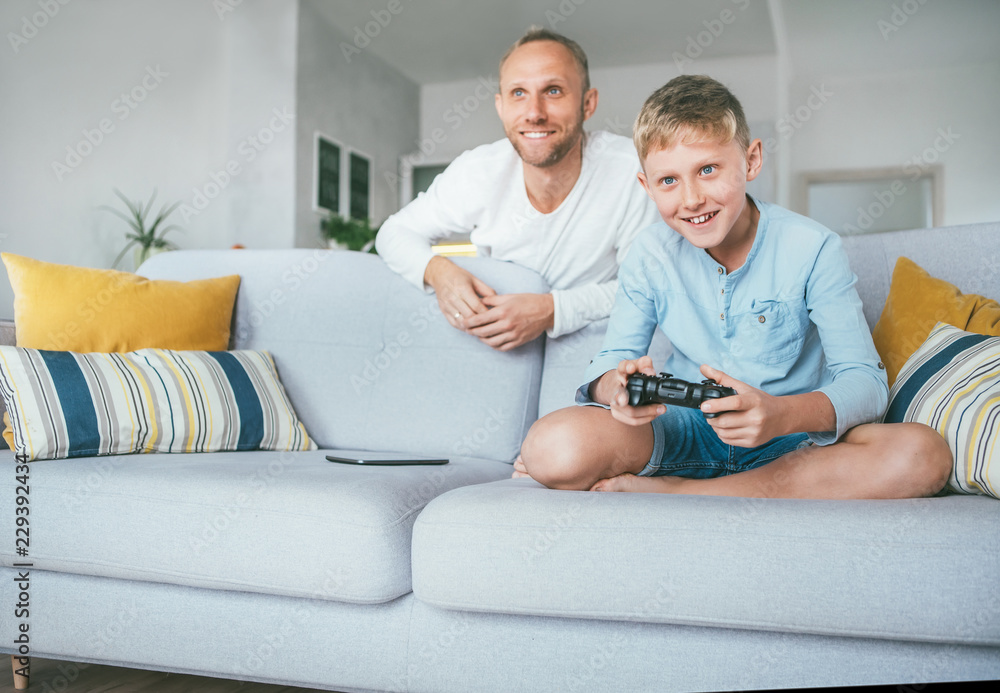 Father watching his son playing TV video game using the gamepad Father watching his son playing TV video game using the gamepad
