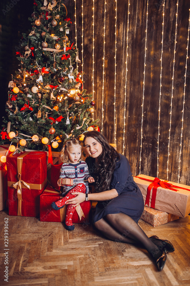 Portrait of beautiful mother and dauther near the Christmas tree. Family woman with little child in a festive New Year's atmosphere. Happy holiday moment. Portrait of beautiful mother and dauther near the Christmas tree. Family woman with little child in a festive New Year's atmosphere. Happy holiday moment.