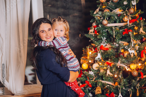 Portrait of beautiful mother and dauther near the Christmas tree. Family woman with little child in a festive New Year's atmosphere. Happy holiday moment.