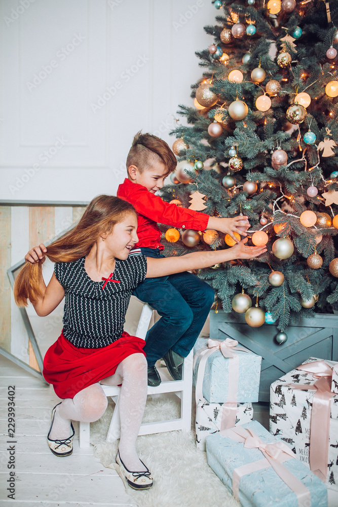 Happy little kids decorate Christmas tree in beautiful living room, Funny  christmas moment. Children opening presents on Christmas eve. Holiday gifts  for kid. Stock Photo