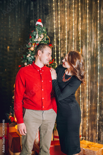 Middle age couple near Christmas tree. Smiling woman holding her partner from behind while spending happy moments celebrating. Christmas moments