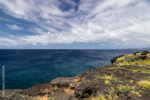 View from South Point on the Big Island of Hawaii. This is the southernmost point in the United States. Past the lava rock cliff is the deep blue pacific Ocean  blue sky and clouds in the distance.  © dhayes