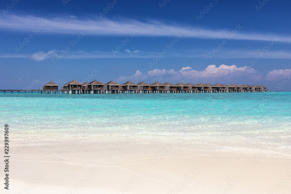 Tropischer Paradies Strand mit türkisem Meer, feinem Sand und Wasser Bungalows als Hintergrund