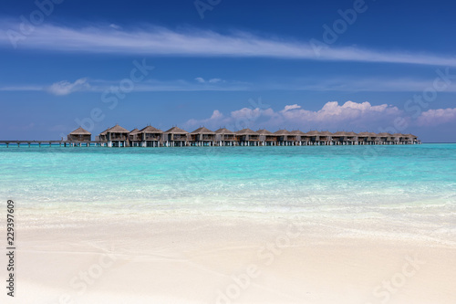 Tropischer Paradies Strand mit türkisem Meer, feinem Sand und Wasser Bungalows als Hintergrund