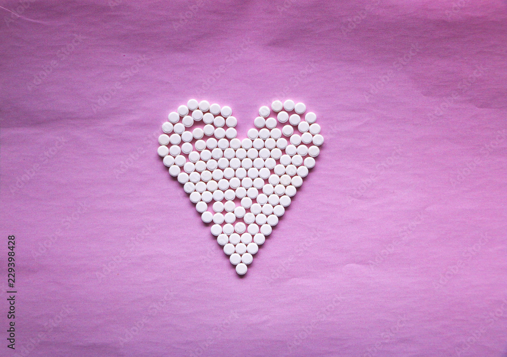 white pills laid out in the shape of a heart on a pink background. concept - heart disease, heart disorders and drugs, cardiology.