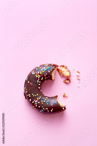 Half eaten donut with chocolate coating and sprinkles on a pink background viewed from above. Sweet food leftovers. Top view. Copy space