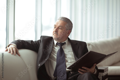 pensive businessman with clipboard sitting on the office couch