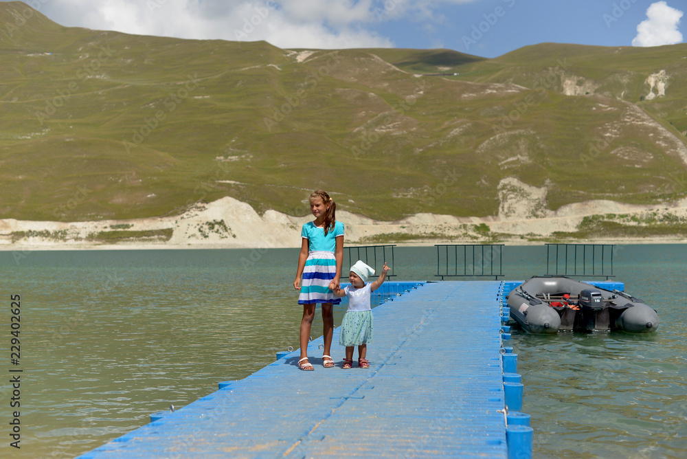 Beautiful mountain blue lake in the Chechen Republic. Sister girls walking on the pier.