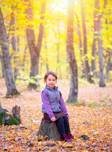beautiful little girl stands on a trunk of tree smiling