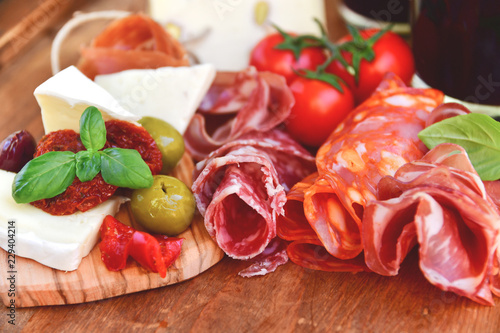 Traditional italian antipasto with prosciutto, parmesan cheese and brie cheese, sun-dried tomatoes, salami, green olives and Basil, wooden table, Italian restaurant, selective focus