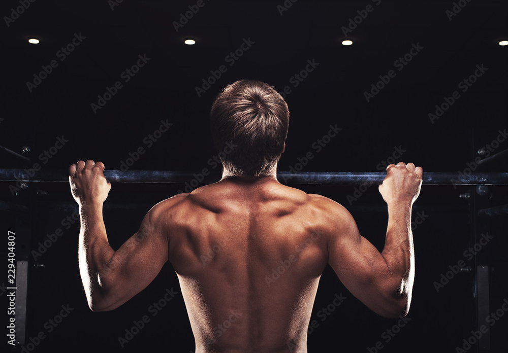 Rear view of muscular man doing pull up exercise on horizontal bar. Male athlete working out in the gym Rear view of muscular man doing pull up exercise on horizontal bar. Male athlete working out in the gym