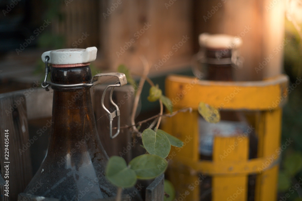Two big brown glass bottles in wooden containers an autumn evening Two big brown glass bottles in wooden containers an autumn evening