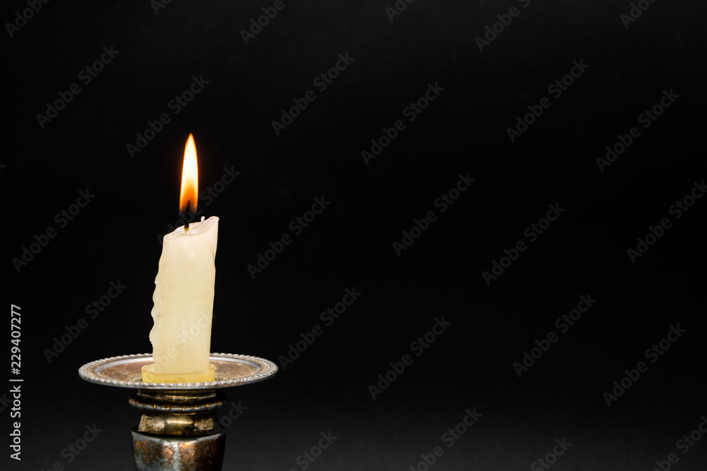 Lighted candle in an old candlestick on a black background Lighted candle in an old candlestick on a black background