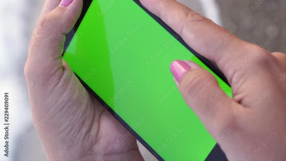 Vertical closeup video of woman's hands scrolling virtual website at mobile smartphone with blank green screen in vertical position isolated on sea water and sandy beach background. Mock up. Vertical closeup video of woman's hands scrolling virtual website at mobile smartphone with blank green screen in vertical position isolated on sea water and sandy beach background. Mock up.