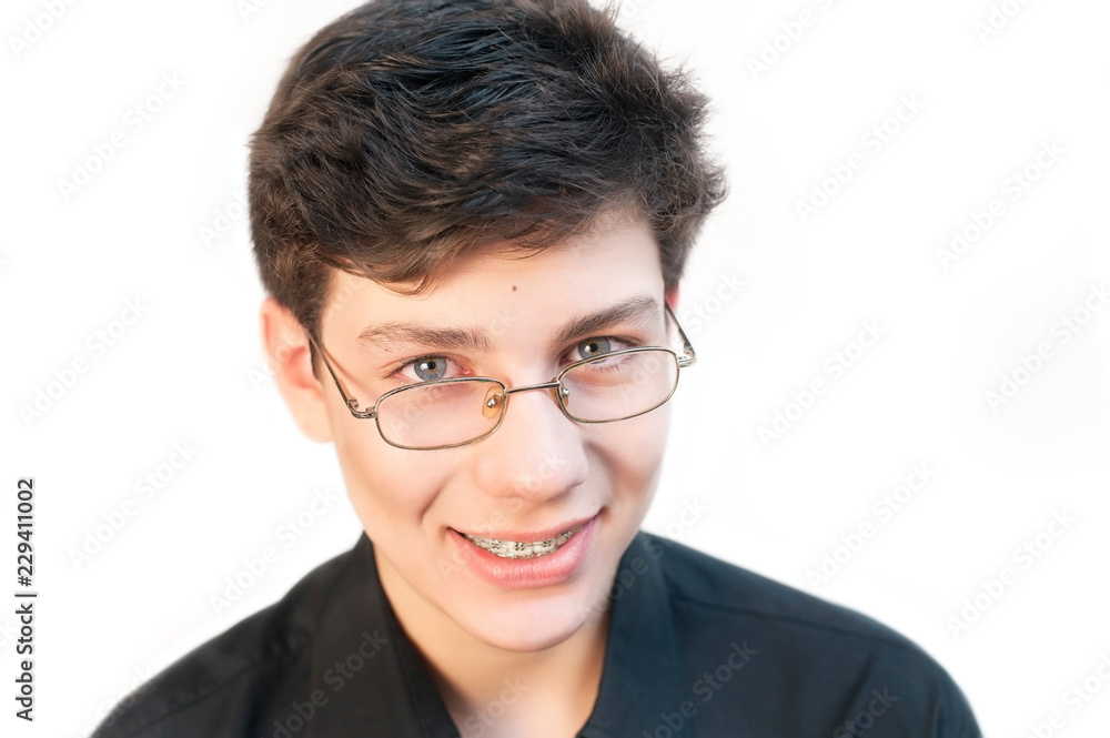 Beautiful guy on a white background in a black shirt with glasses to improve his eyes smiles with braces on his teeth