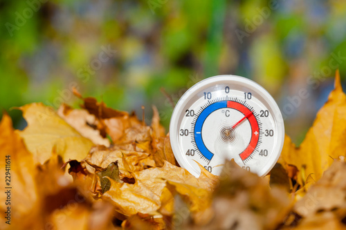 Outdoor thermometer in golden maple leaves shows warm temperature - hot indian summer concept photo