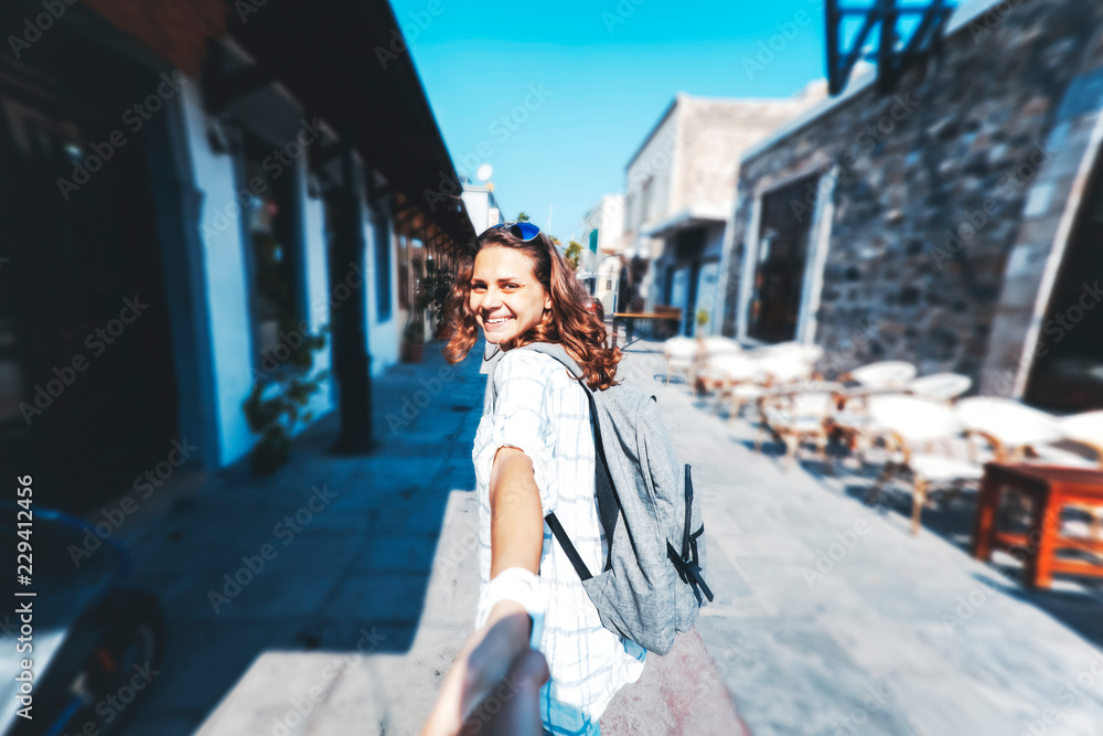 Look from behind at young woman holding man's hand in 'Follow me' pose, young cute female traveler with backpack