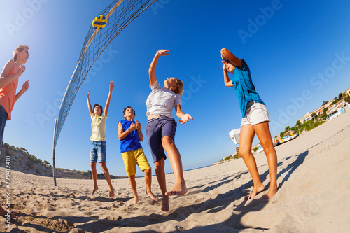 Excited boys and girls playing beach volleyball