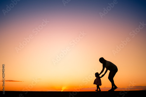 Fototapeta Naklejka Na Ścianę i Meble -  Silhouette of mother teaching her child to walk.