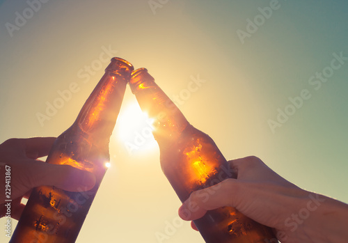 Canvas Print Hands toasting beer on sunset background