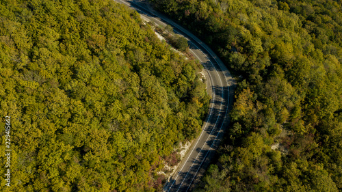 Aerial view of curvy rural road in mountains in autumn season. Cars driving below on the road.