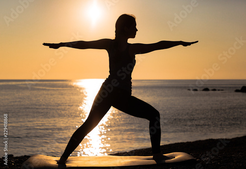 Asana warrior at the sunset. Women practicing yoga on the beach