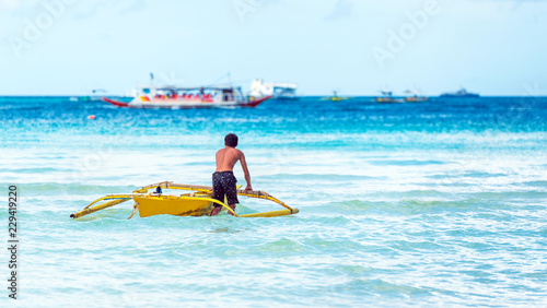 A man with a boat near the shore, Boracay, Philippines. Copy space for text. Back view.