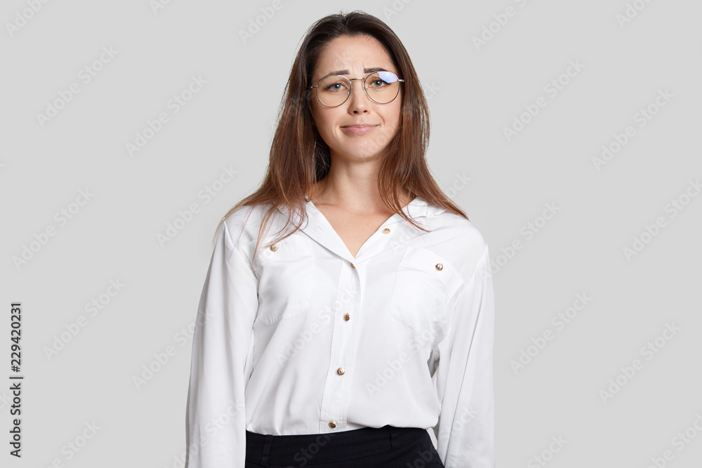 Horizontal shot of displeased European woman with dark hair, wears transparent glasses, formal clothes, looks in discontent, recieves much tasks from employer, isolated over white background Horizontal shot of displeased European woman with dark hair, wears transparent glasses, formal clothes, looks in discontent, recieves much tasks from employer, isolated over white background