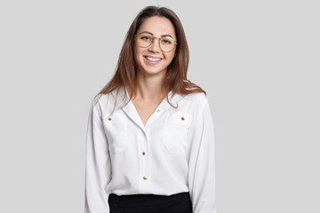 Indoor shot of pleasant looking smiling young female architect wears transparent round glasses, formal outfit, rejoices promotion at work, isolated over white background. People and work concept