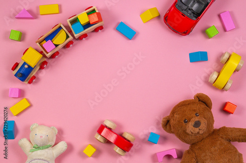Baby kids toys frame with teddy bear, toy car, wooden train, colorful bricks on pink background. Top view