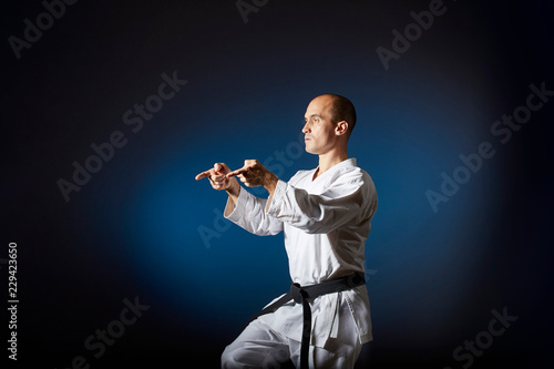 Adult athlete performs formal karate exercises on blue background with gradient